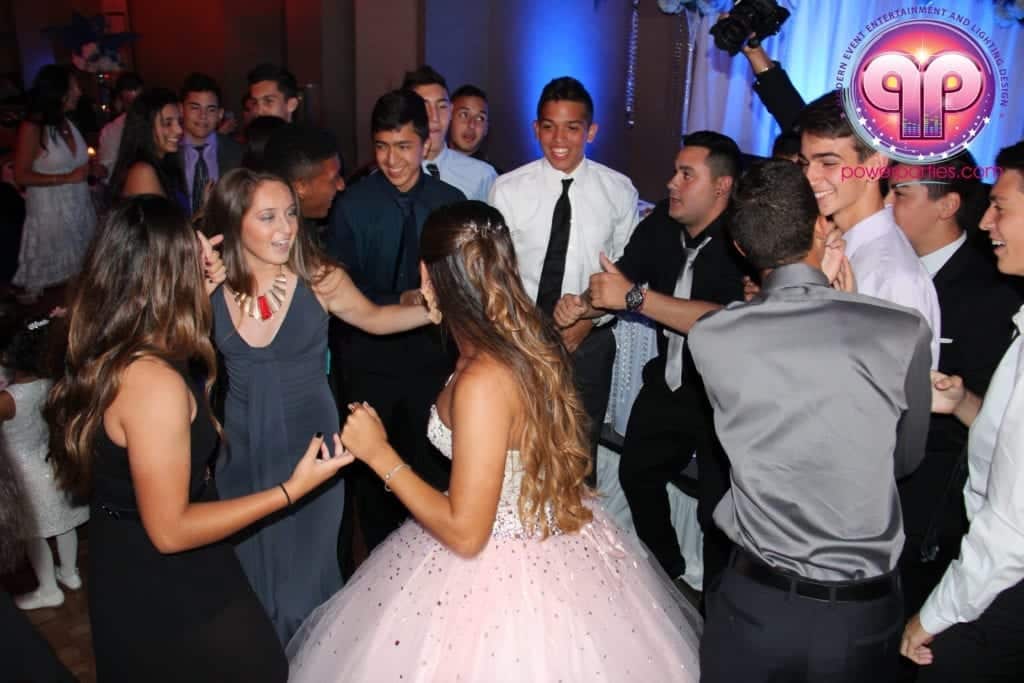 Jóvenes bailando con atuendo formal en una animada fiesta de bodas en Miami, con especial atención en una chica con un vestido rosa brillante, rodeada de amigos disfrutando del momento. By www.powerparties.com